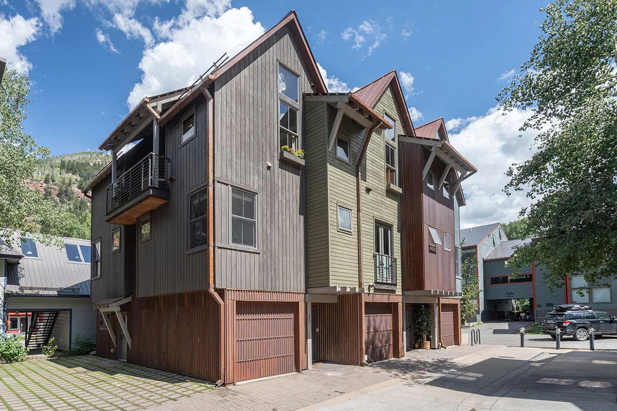 A modern home exterior with a textured facade, striking architectural lines, and lush greenery. The balcony hints at inviting outdoor living, ideal for relaxing after a day’s adventure. Surrounding paths and landscaping suggest easy access to nearby trails.
