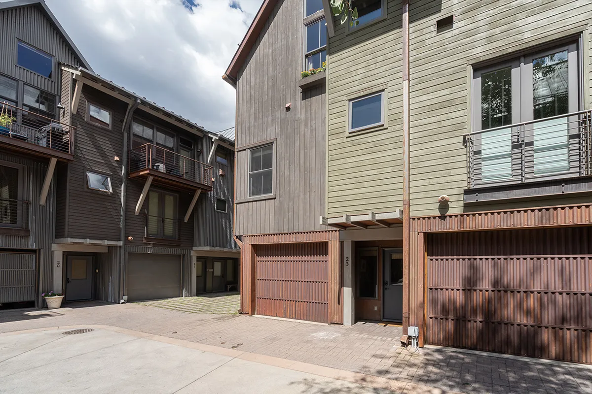 A modern townhouse exterior with clean architectural lines, featuring balconies adorned with plants. The scene evokes a sense of welcoming community and contemporary living, with garage doors and a well-maintained facade hinting at family-friendly residential comfort.