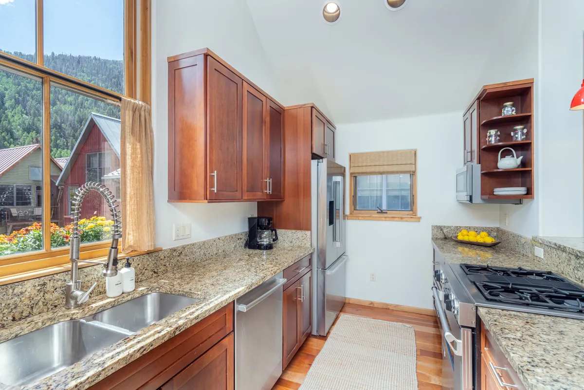 A chef-inspired kitchen featuring granite countertops, wooden cabinetry, stainless steel appliances, and large windows that let in ample sunlight and provide mountain views. The kitchen is spacious and designed for both meal preparation and gathering with loved ones.