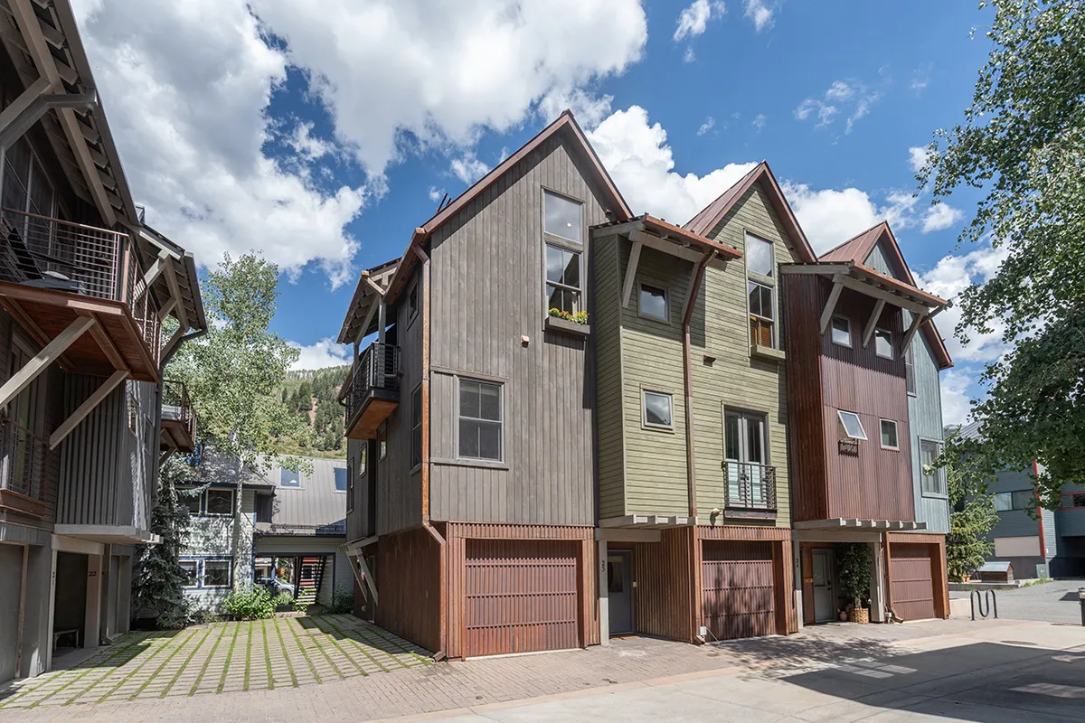 A modern building exterior with colorful facades and balconies adorned with plants, suggesting outdoor relaxation and a welcoming, community-oriented vibe. The scene evokes evening strolls or casual socializing steps from the front door.