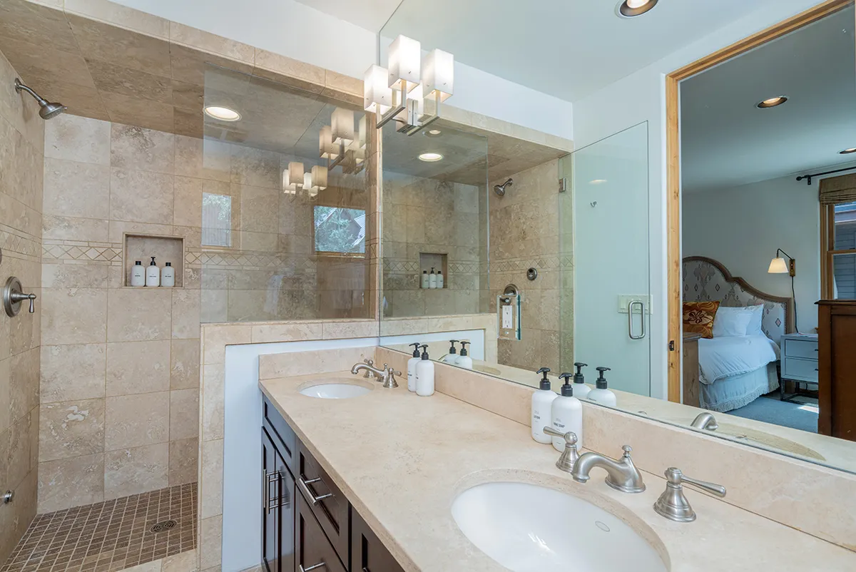 A spacious bathroom with a double sink vanity, a walk-in shower, a large mirror, and natural light streaming in from a window. The finishes are modern and clean, creating a tranquil and refreshing environment.